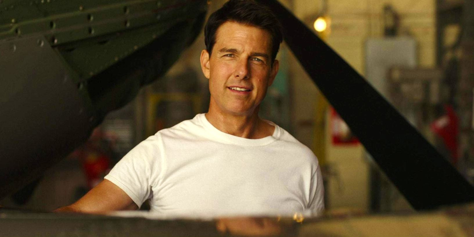Tom Cruise as Maverick wearing white shirt and standing by plane in Top Gun: Maverick