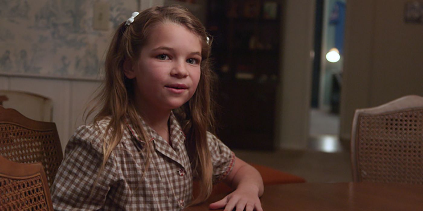 Uma jovem Missy de Young Sheldon sentada na cozinha, com a mão na mesa.