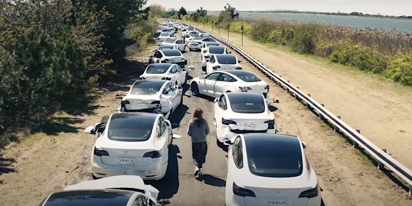 A woman walks alone between two long lines of white cars blocking a country road along the sea