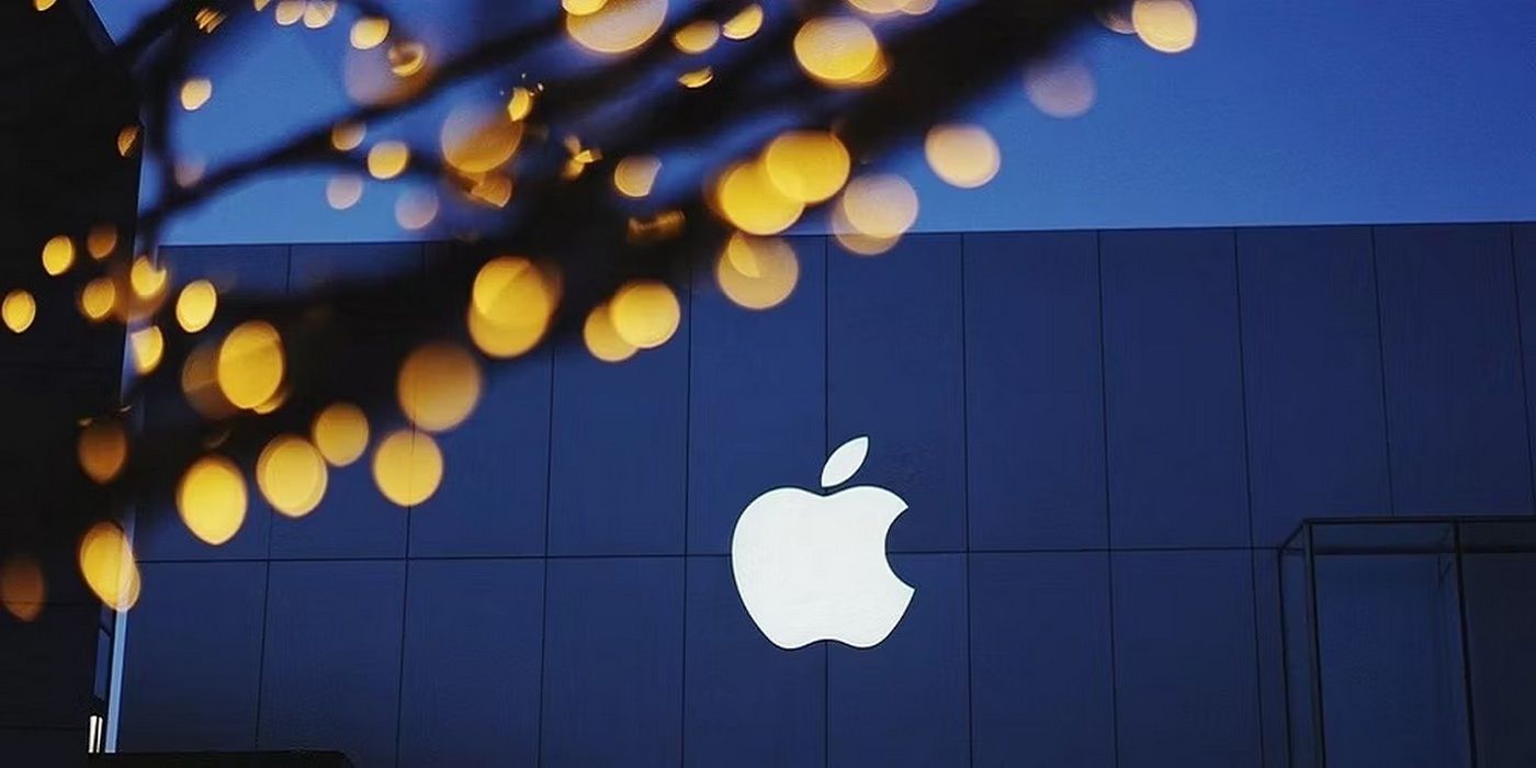 White Apple logo with blurred lights in the foreground and a building in the background
