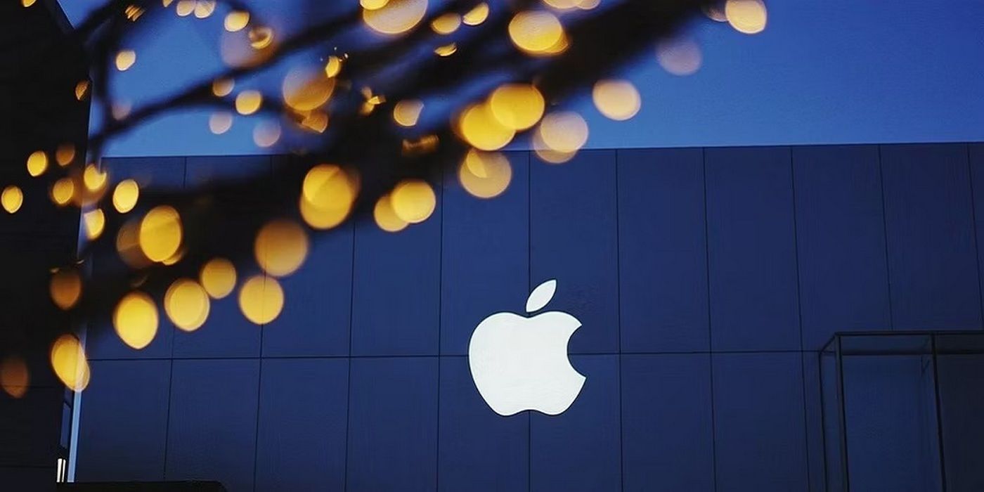 White Apple logo with blurred lights in the foreground with a building in the background