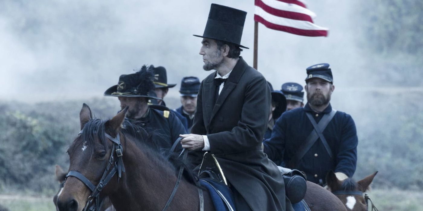 Daniel Day Lewis as Abraham Lincoln in his famous black coat and stovepipe hat sitting atop a horse, followed by mounted soldiers in the Union Army.