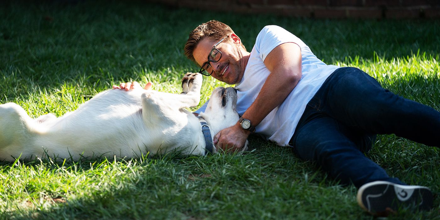 An image of John lying in the grass with a dog in Dog Gone