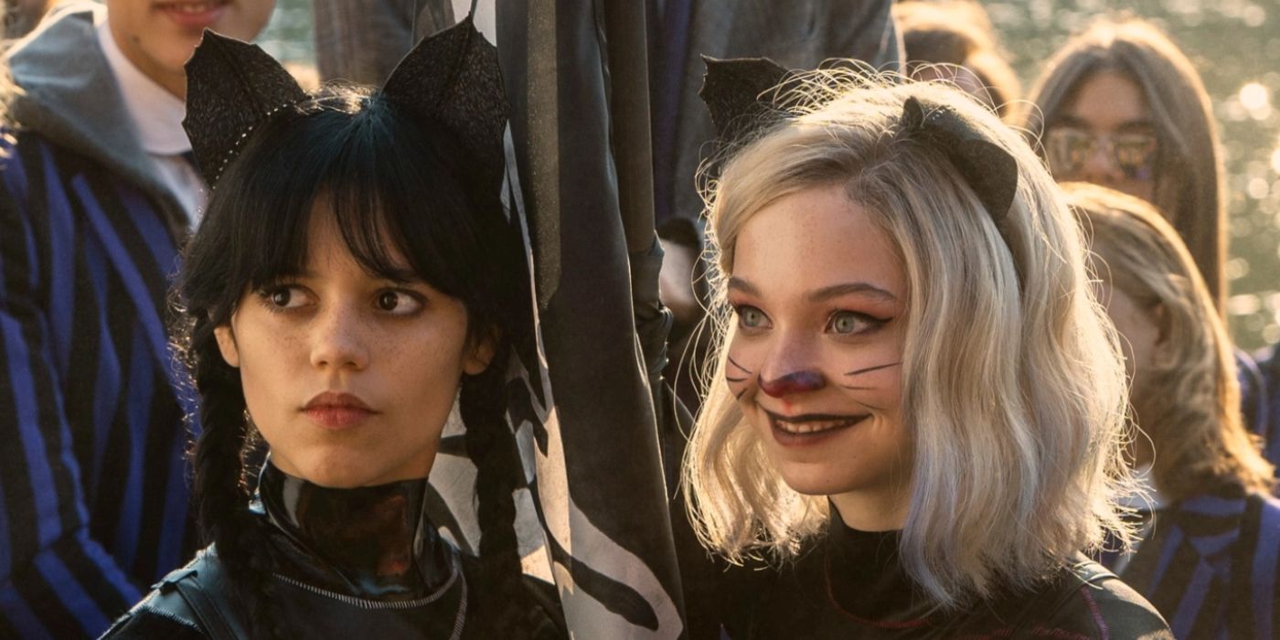 Emma Meyers as Enid grinning and Jenna Ortega as Wednesday deadpan expression in cat makeup