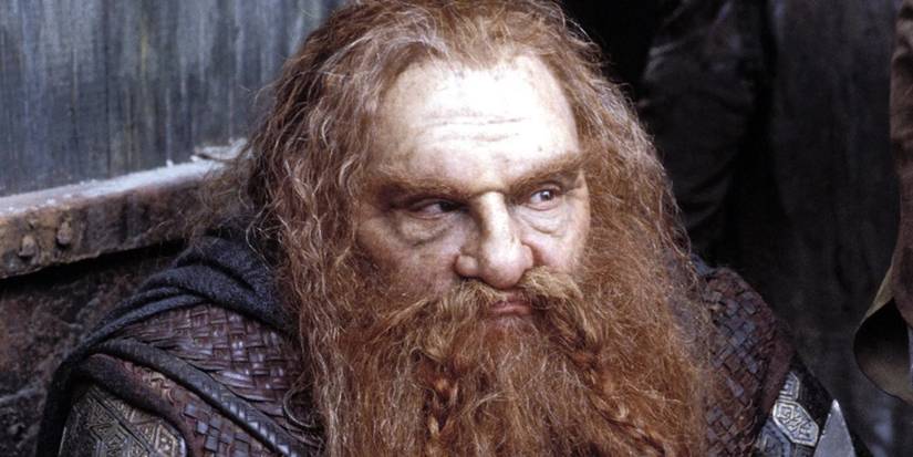 Gimli (John Rhys-Davies) sits looking on sternly and leaning on his axe in the Lord of the Rings films. 