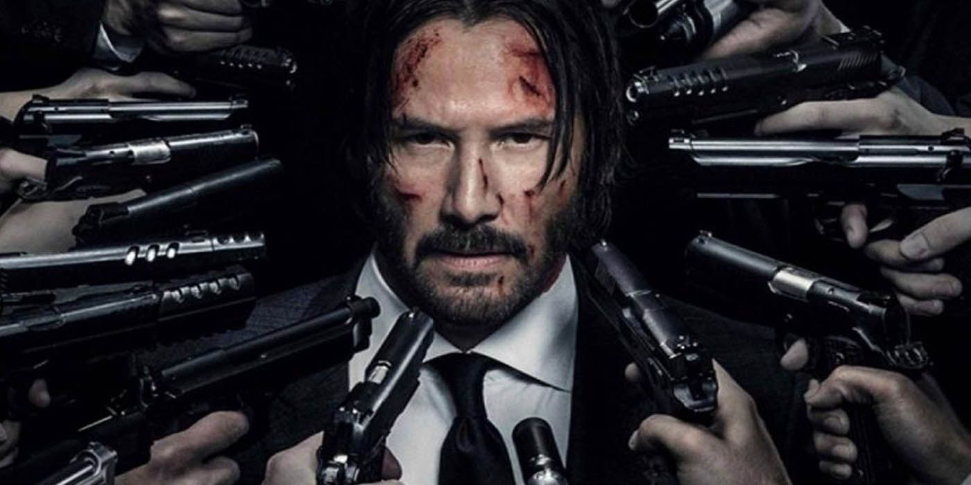 John Wick with blood on his face, surrounded by guns.