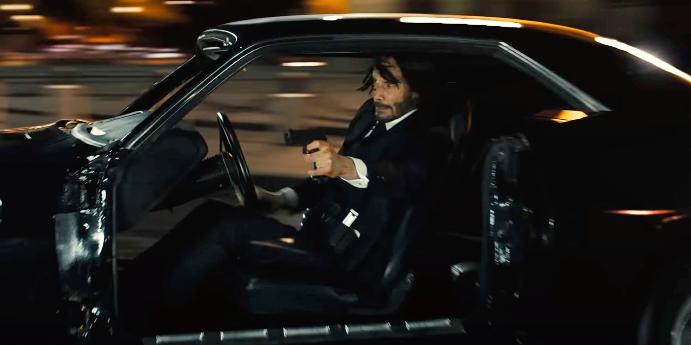 Keanu Reeves shoots a gun while driving a car in John Wick: Chapter 4.