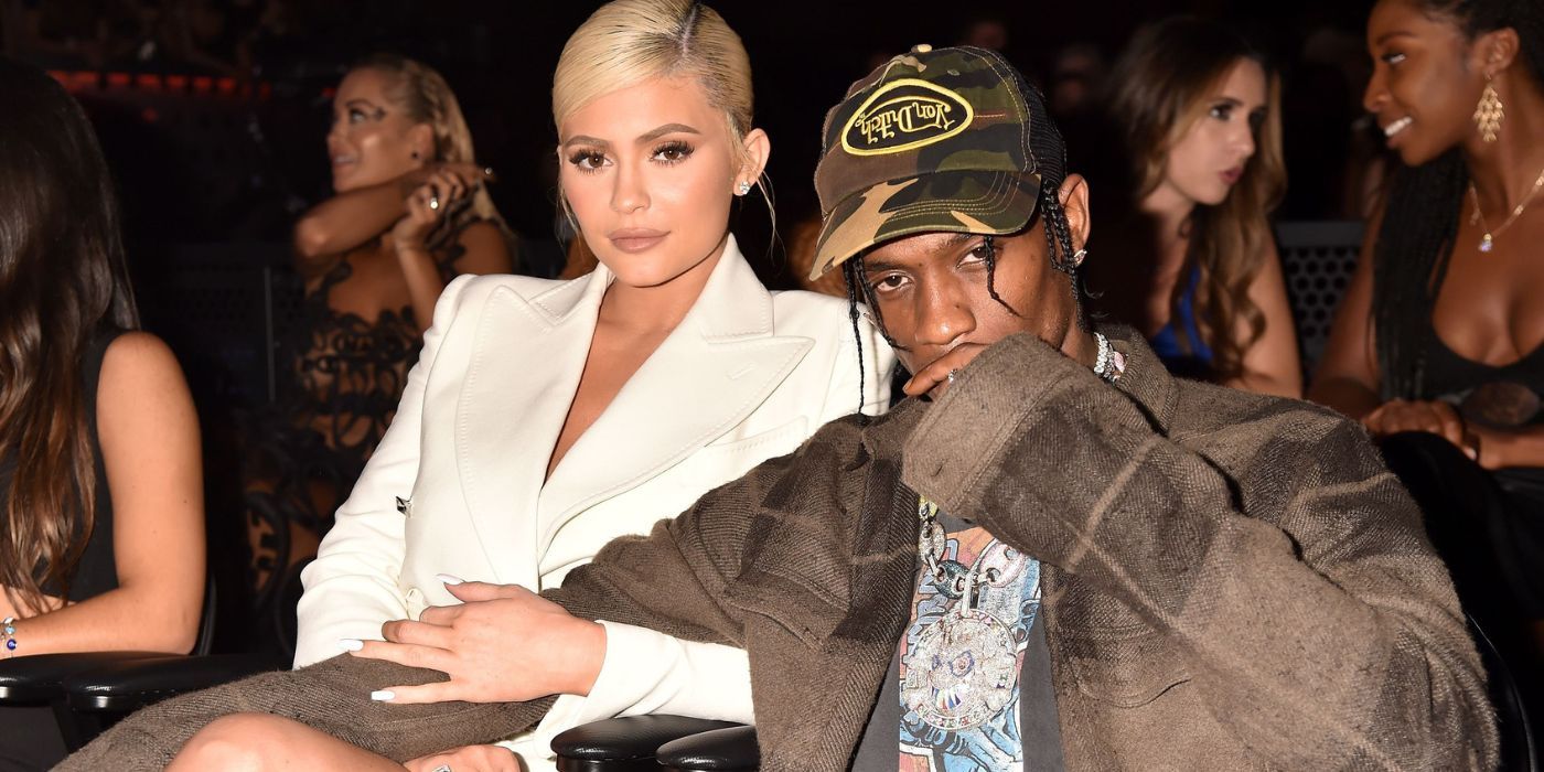 Kylie Jenner and Travis Scott sitting at a fashion show with Kylies arm around Travis looking serious