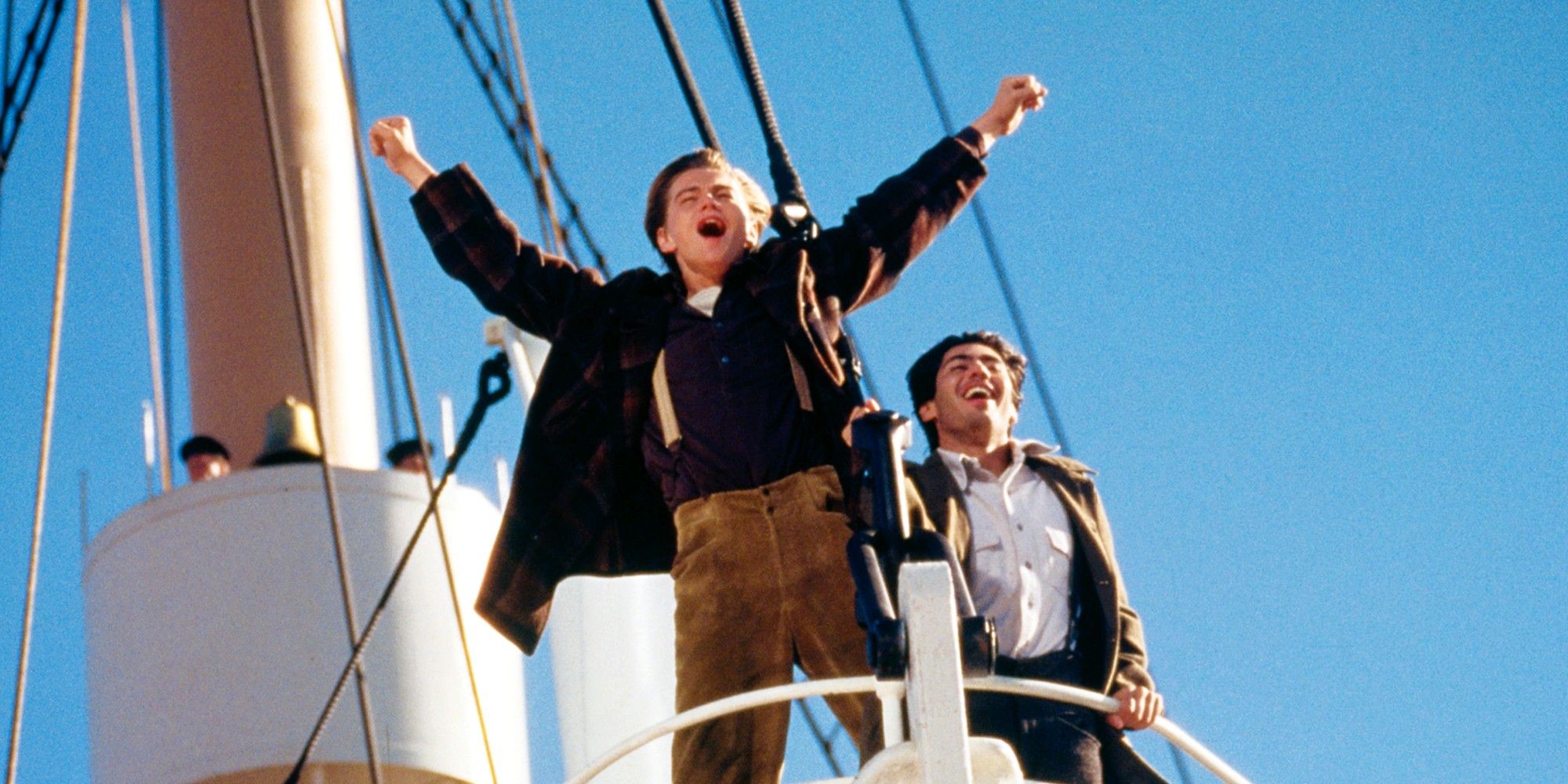 Leonardo DiCaprio como Jack em Titanic parado na proa do navio com os braços no ar e gritando