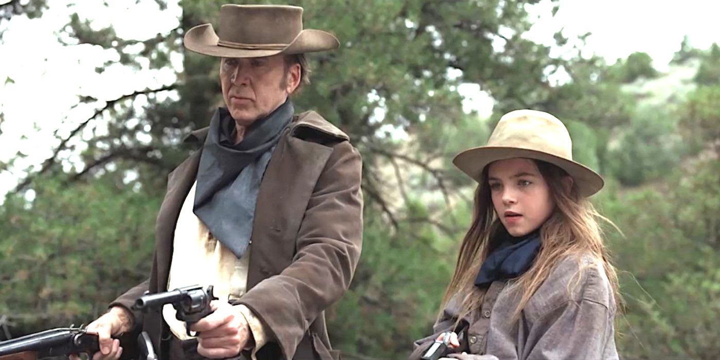 Nicolas Cage in cowboy attire pointing two guns alongside child actor Ryan Kiera Armstrong also dressed in Western costume  and pointing her own weapon