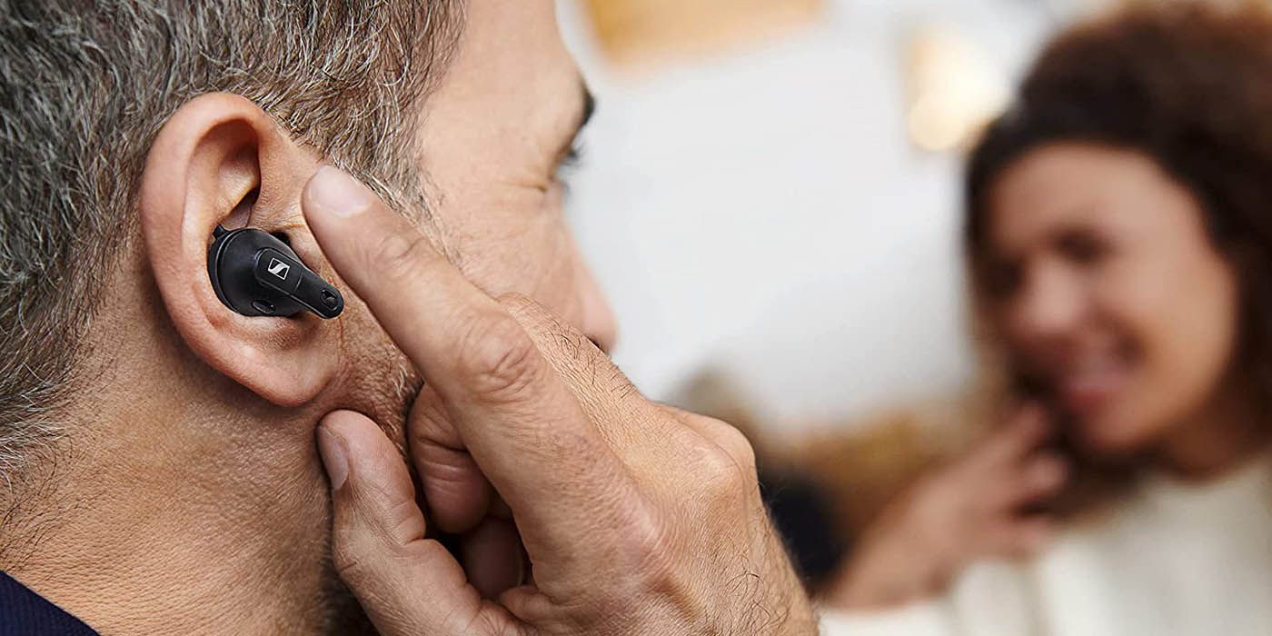 A man wearing the Sennheiser Conversation Clear Plus with his finger on his ear.