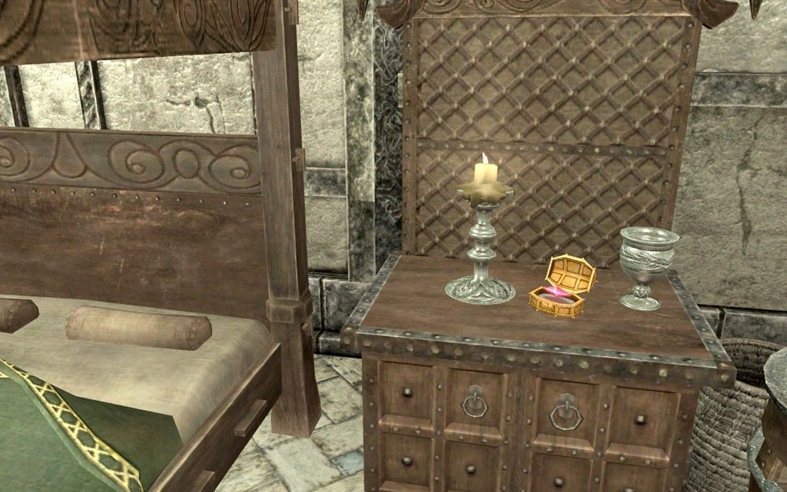A pink Stone of Barenziah in a golden case sitting on a table next to a bed Skyrim.