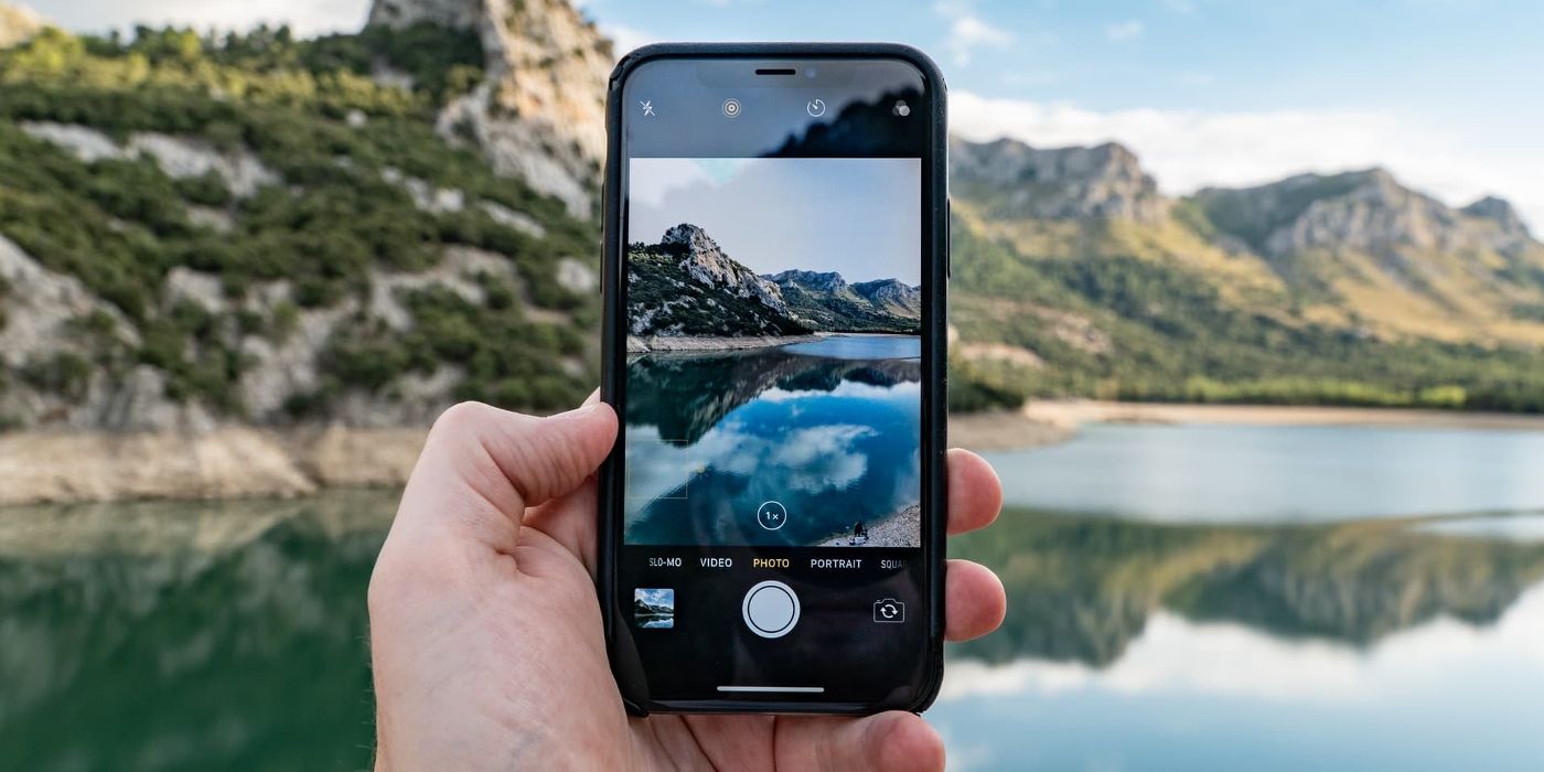 Uma mão segura uma câmera de iPhone à beira de um lago