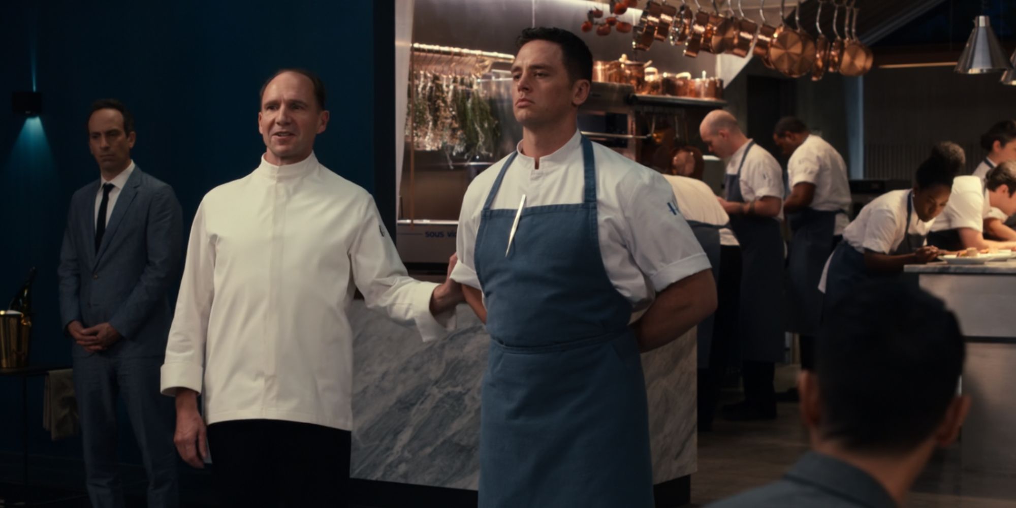 Julian (Ralph Fiennes) standing with a man in an apron in The Menu