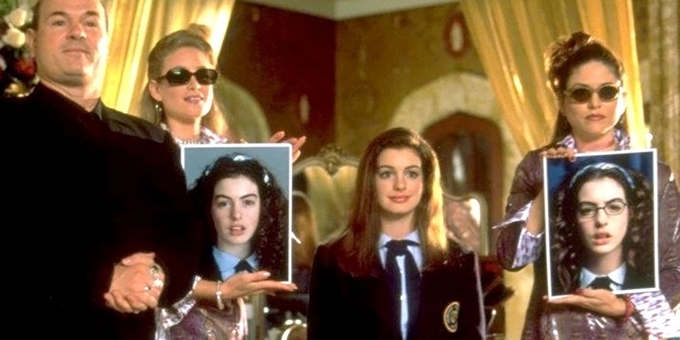 Two women hold up old pictures of Mia as she looks in a mirror in The Princess Diaries