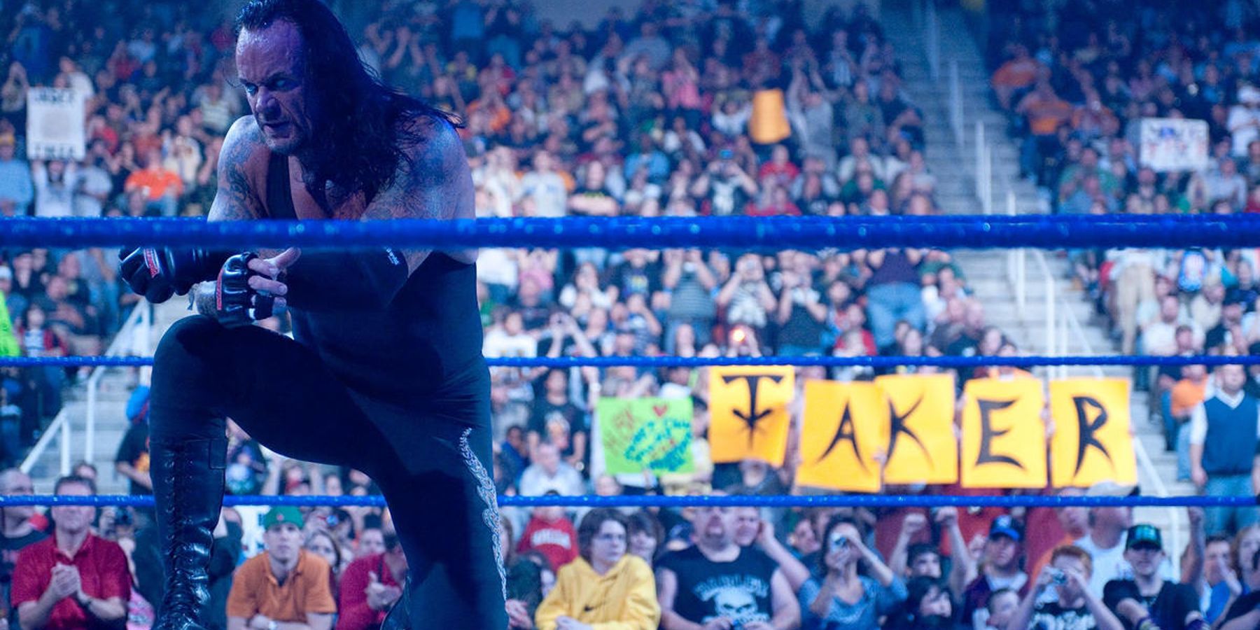 The Undertaker poses for the crowd while fans in the backround hold up a sign in support of him.