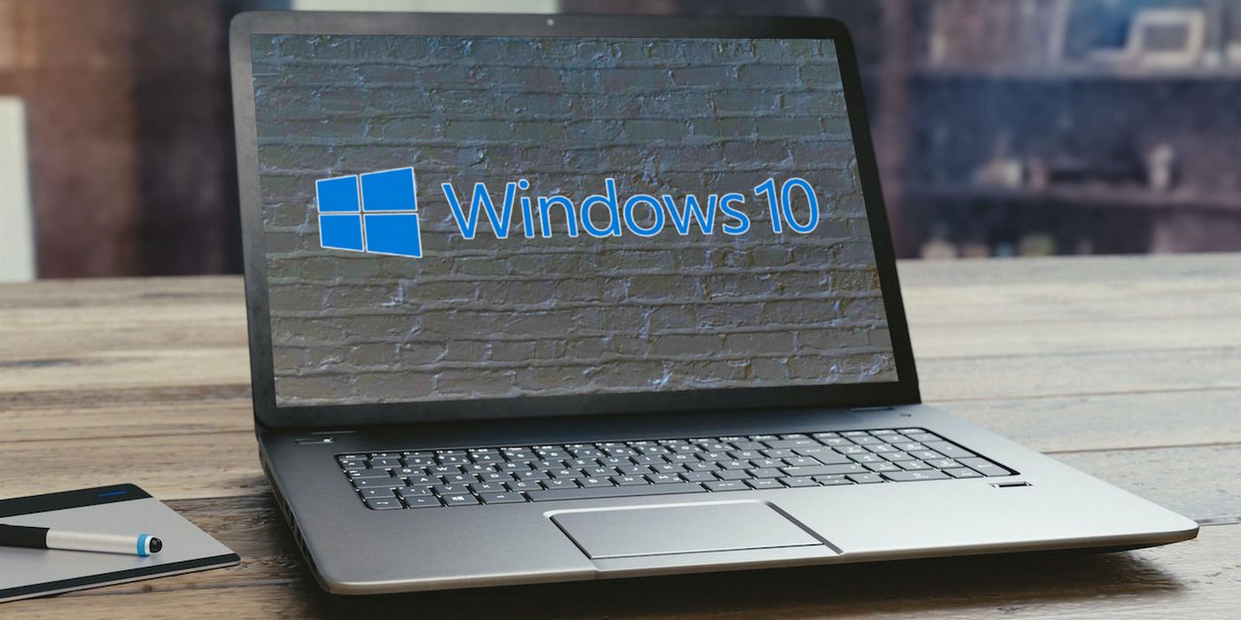 An open laptop with a wallpaper that depicts a Windows 10 logo on a gray brick wall.