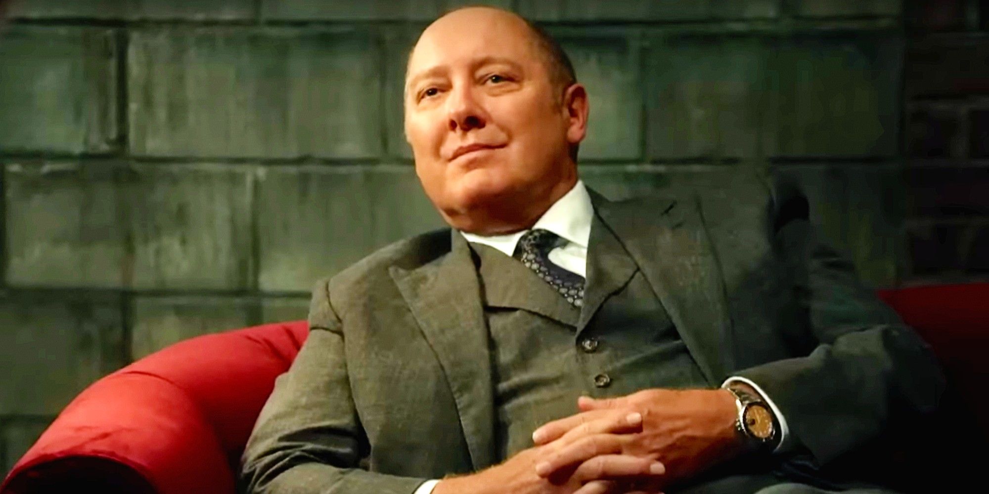 James Spader in The Blacklist sitting in a plush red chair with his fingers laced in his lap