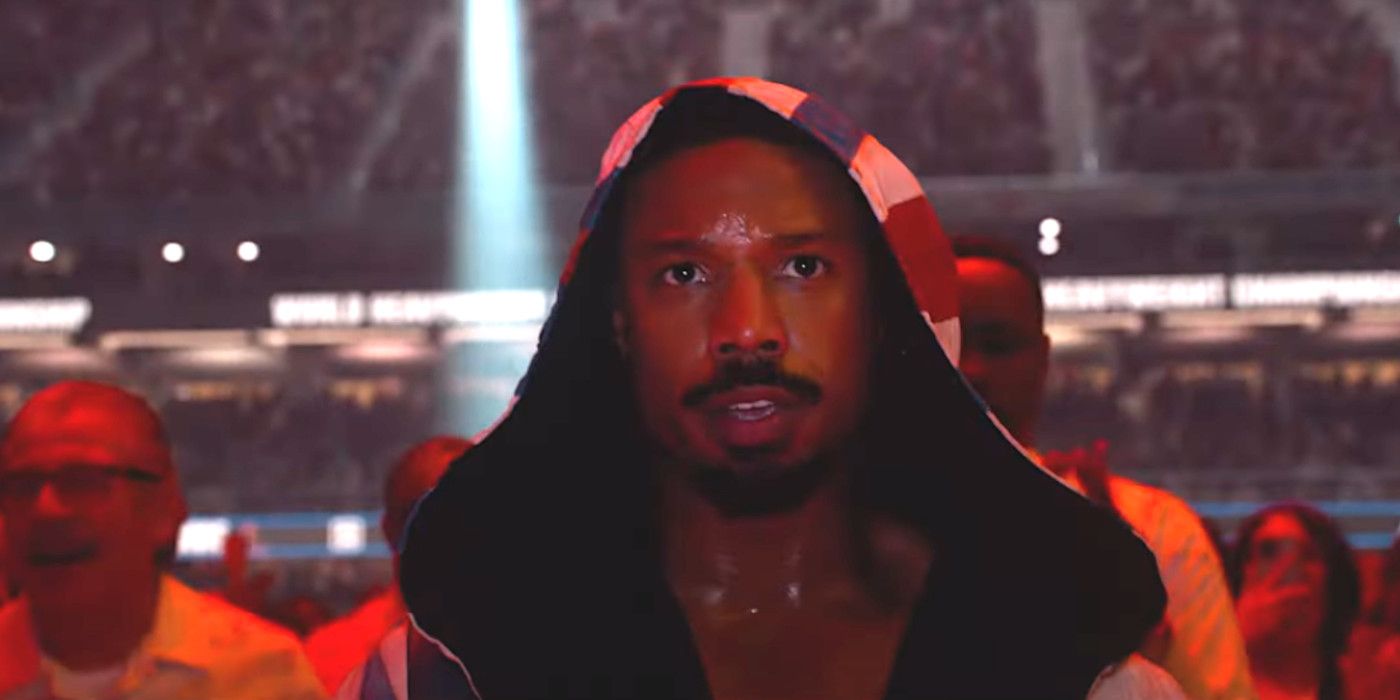 Michael B. Jordan in Creed 3, wearing a robe flooded with red light, enters the boxing ring surrounded by a cheering crowd