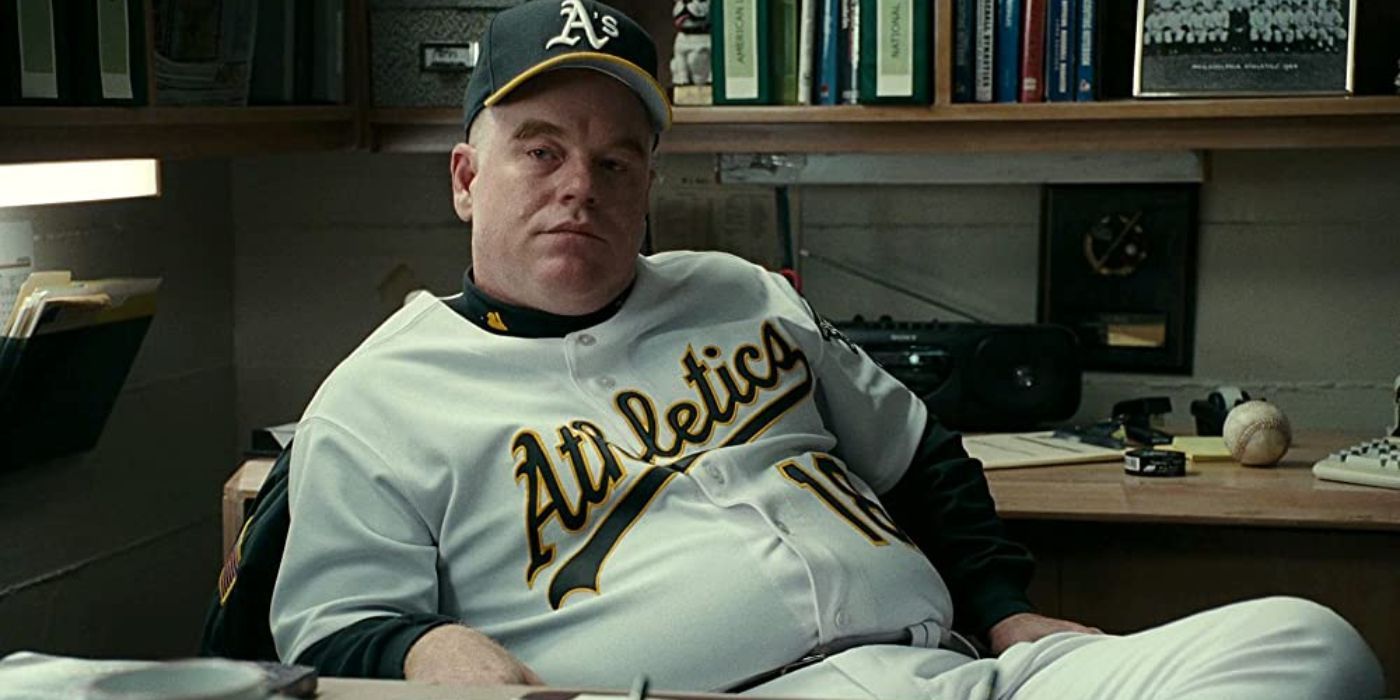 Phillip Seymour Hoffman sitting at a desk in a baseball jersey in Moneyball