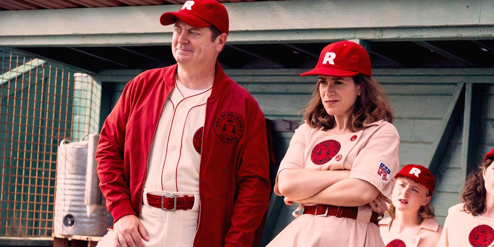 Nick Offerman and Abbi Jacobson in baseball uniforms standing in a dugout on A League of Their Own