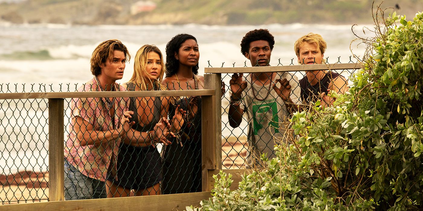 John B, Sarah, Cleo, Pope y JJ mirando por encima de una valla en la temporada 3 de Outer Banks.