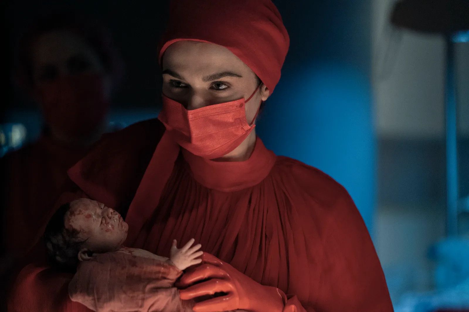 Rachel Weisz in Dead Ringers in a red surgeon's gown holding a newborn baby