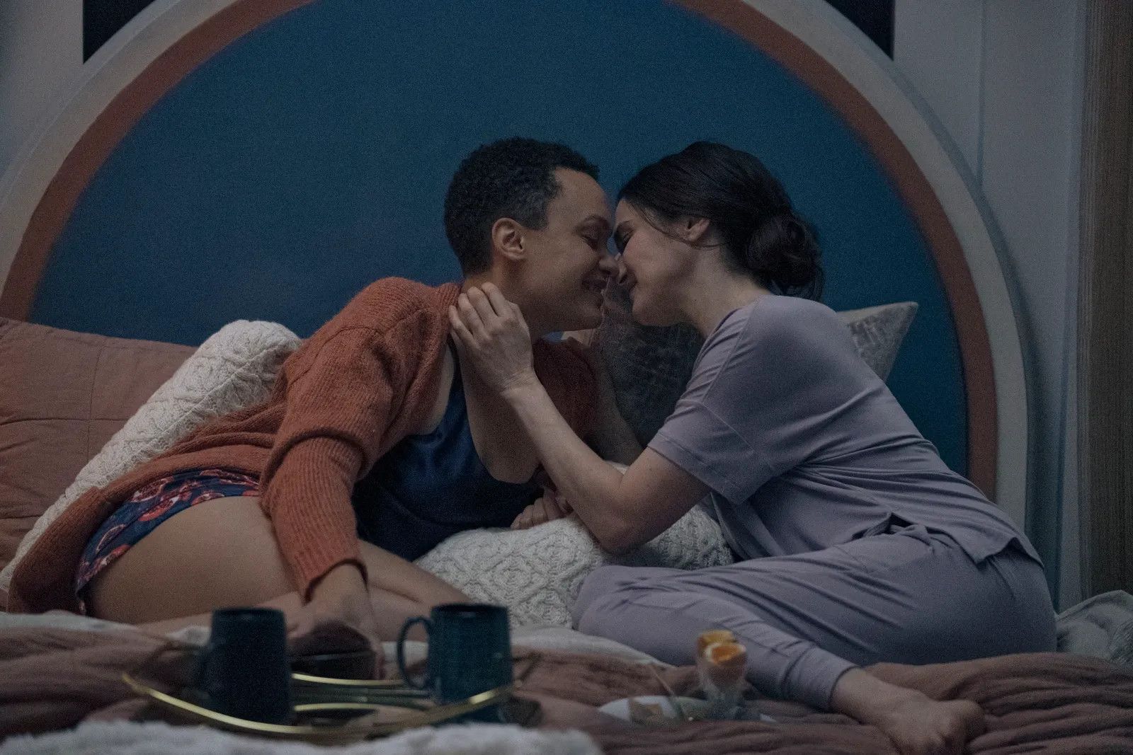 Rachel Weisz and Britne Oldford lying in bed together kissing while plates and cups set at their feet