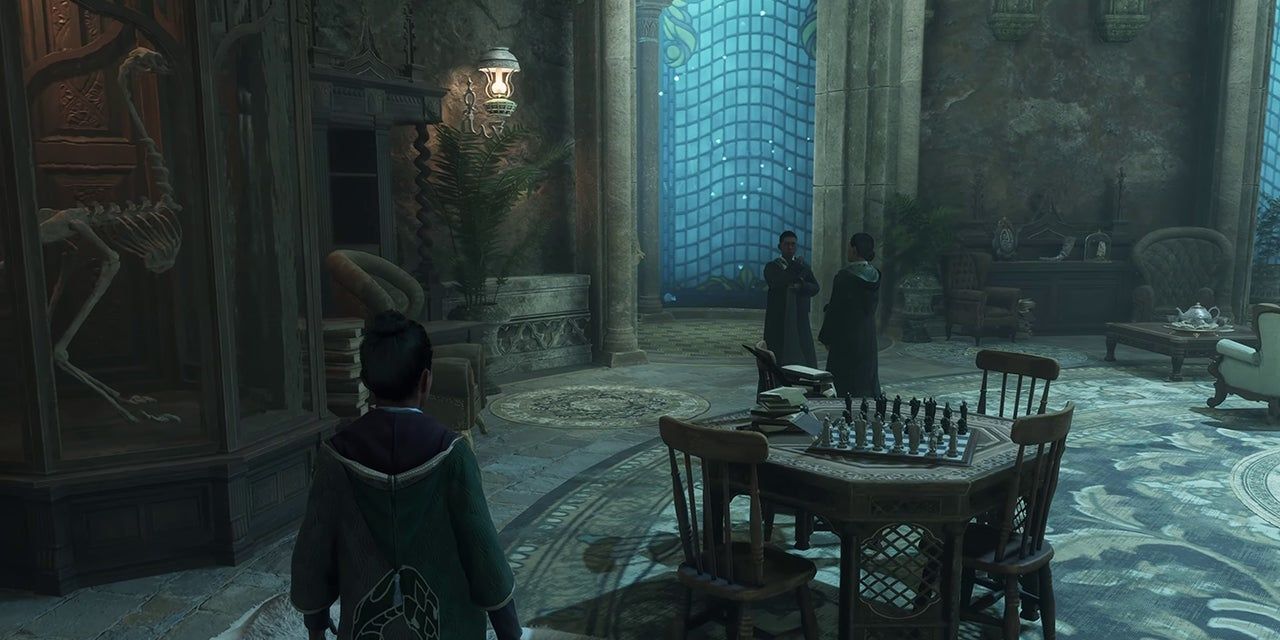 Sala Comunal da Sonserina em Hogwarts Legacy.  Personagem do jogador entrando, um esqueleto de criatura em uma caixa de vidro à esquerda e uma mesa com um tabuleiro de xadrez e livros à direita.