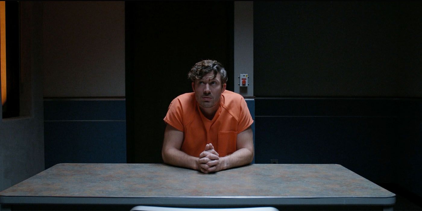 Zach Gilford sitting in a prison jumpsuit in an empty room in Criminal Minds Evolution