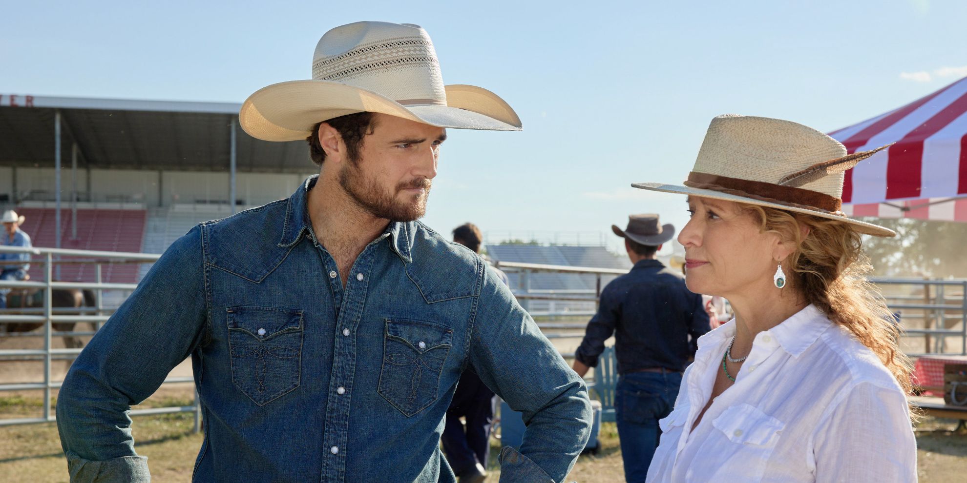 Um homem e uma mulher com chapéus de cowboy olham um para o outro fora de um rodeio na série Hallmark Ride