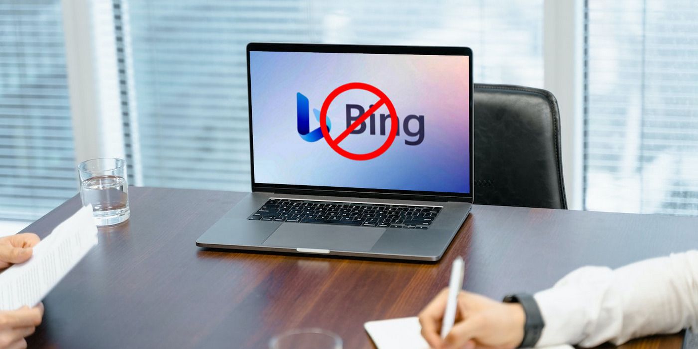A MacBook Pro on a desk, with the display showing a Bing logo superimposed with a 'cancel' sign