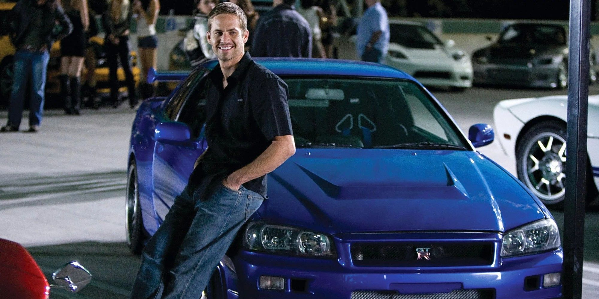 Brian smiling while standing next to his blue Nissan in Fast and the Furious
