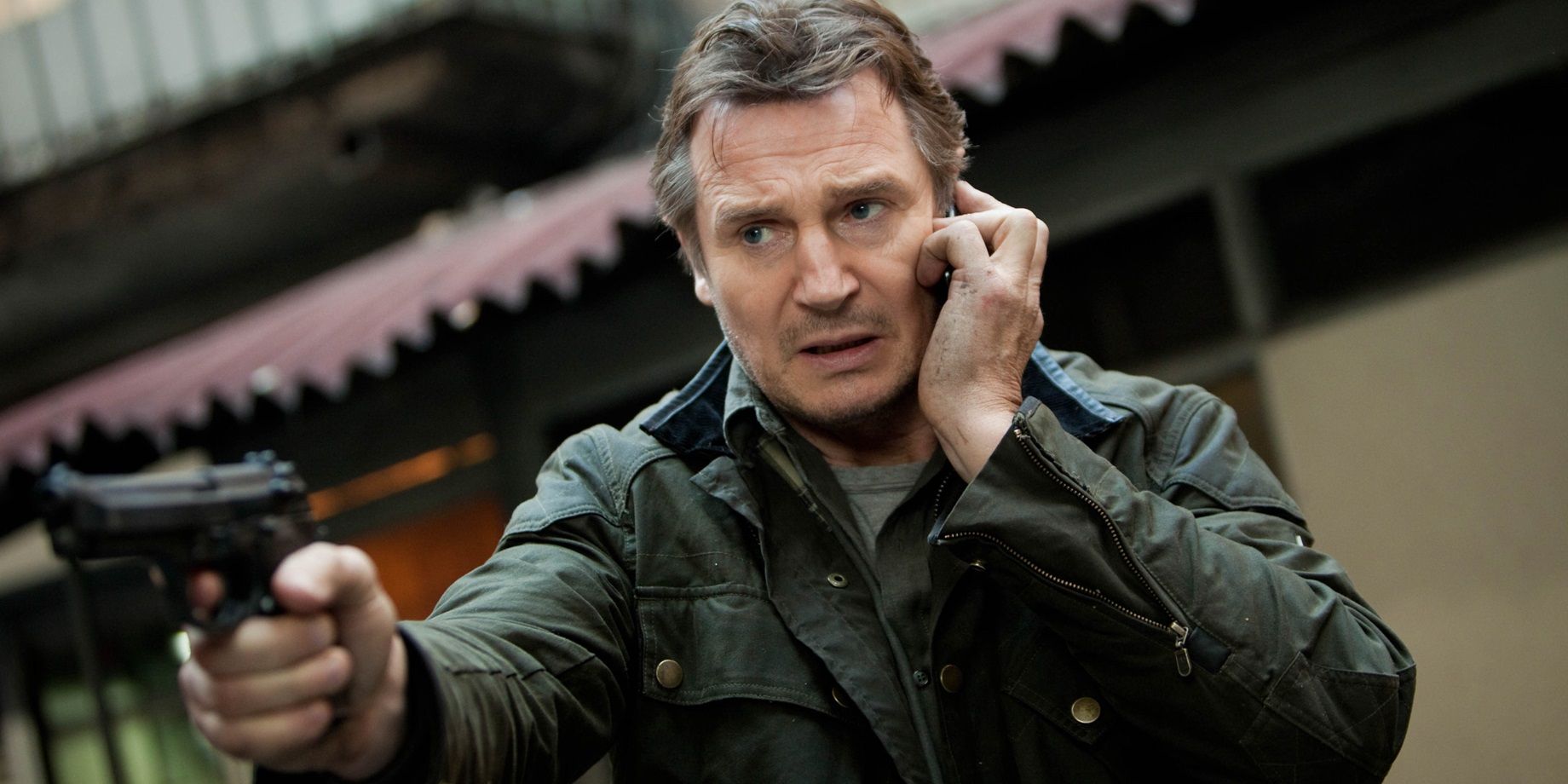 Liam Neeson como Bryan Mills no telefone, mas também segurando uma arma em Busca Implacável 2