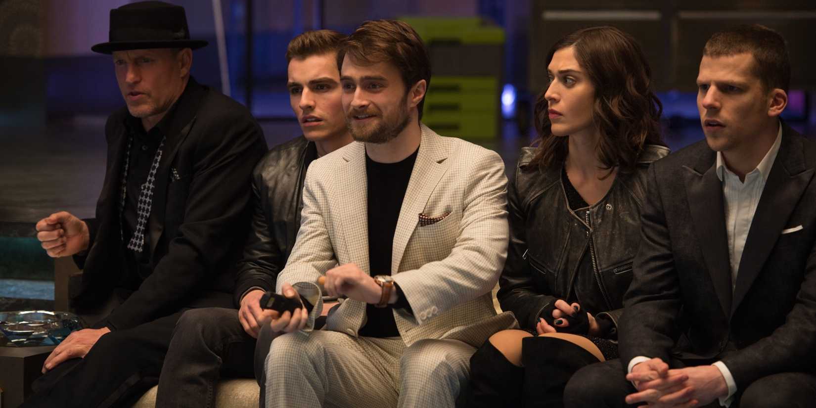 Daniel Radcliffe on a couch turning on the TV with the Four Horsemen looking on in Now You See Me 2