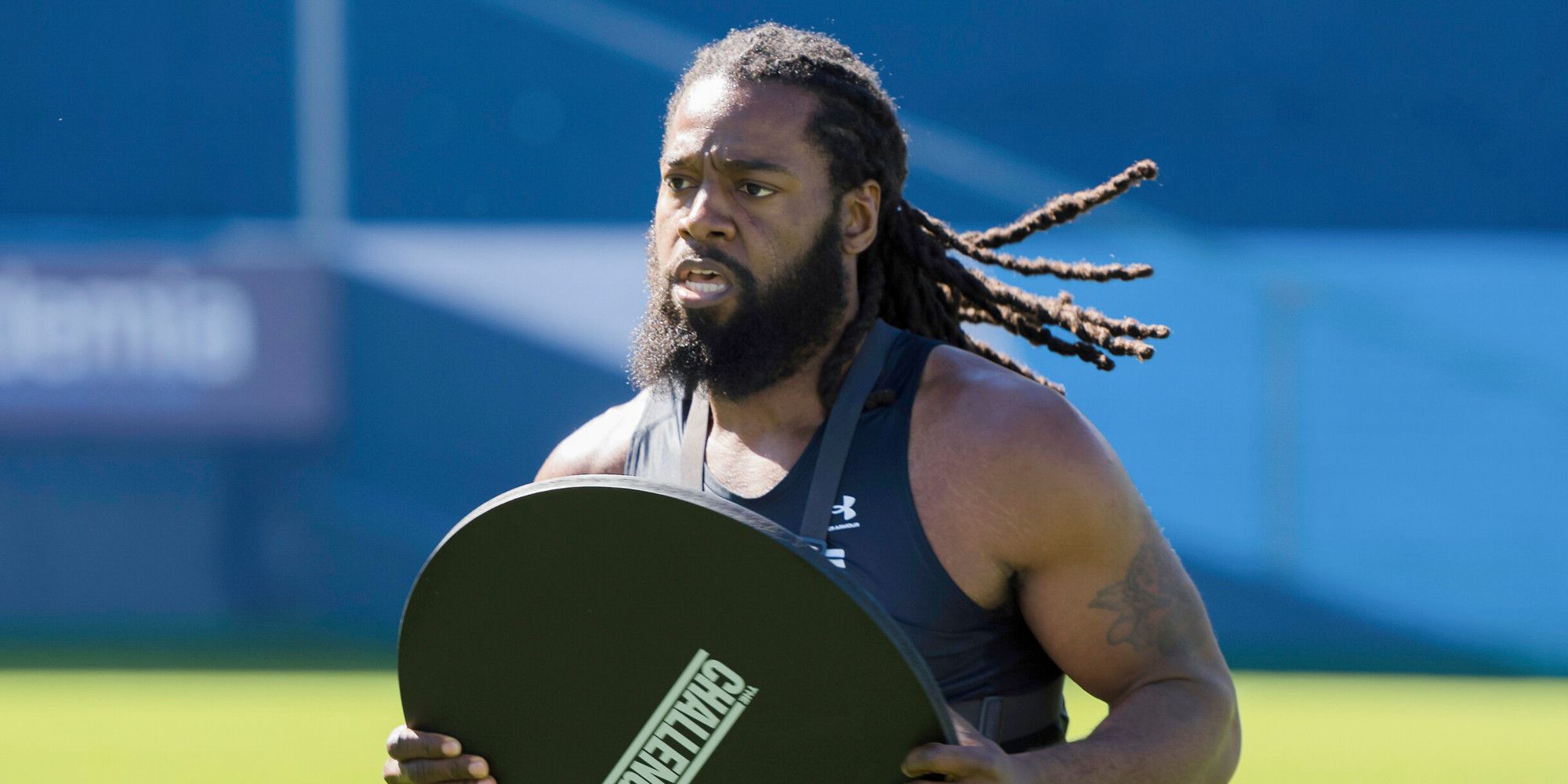 Danny McCray on The Challenge. He is carrying a flat black board and running across a football field.