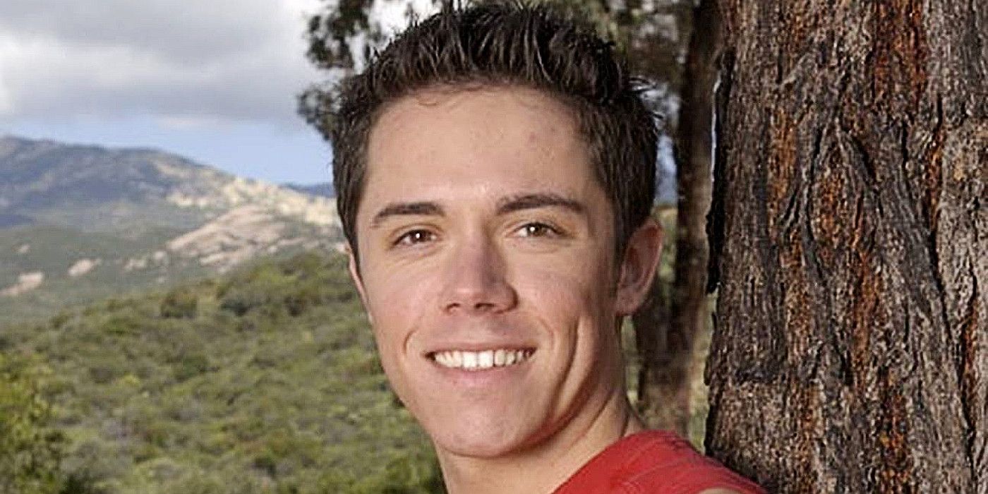 Danny Dias from The Challenge. He is facing the camera, smiling widely, and standing against a tree with a backdrop of hills and greenery behind him.