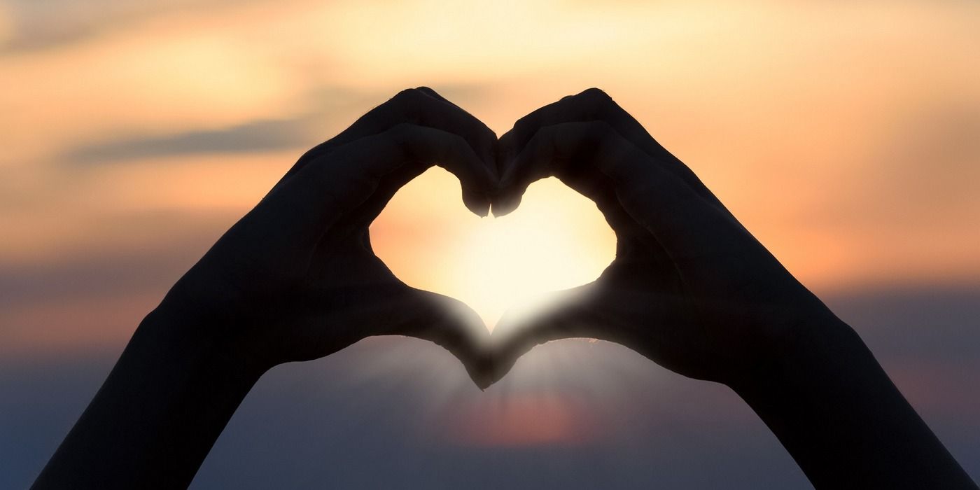 Two hands forming a heart symbol, with a sunset in the backdrop