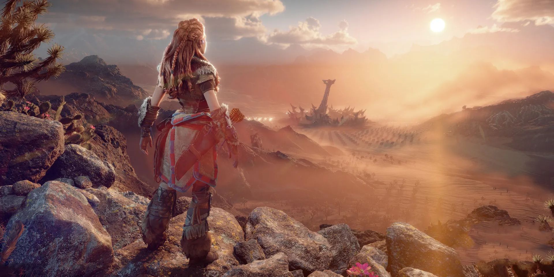 Aloy, standing on a rocky ridge, watches the sun rise or set over a desert landscape in Horizon Forbidden West