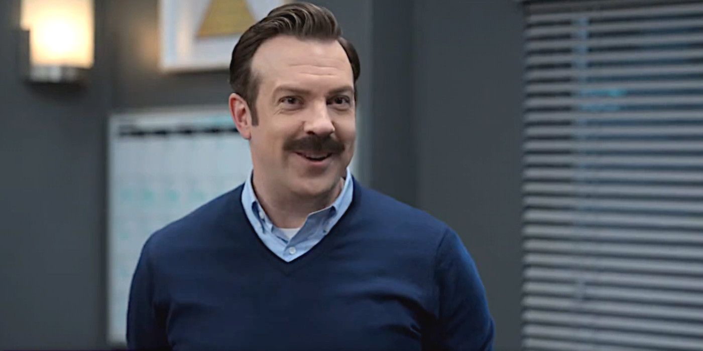 Jason Sudeikis in Ted Lasso Season 3 wearing a blue sweater and having a conversation in an office