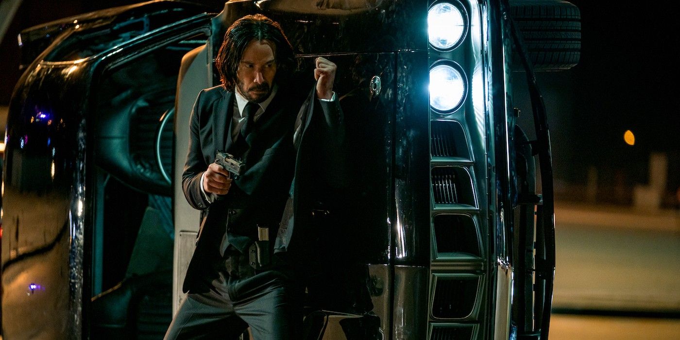 Keanu Reeves hides behind an overturned car in John Wick Chapter 4