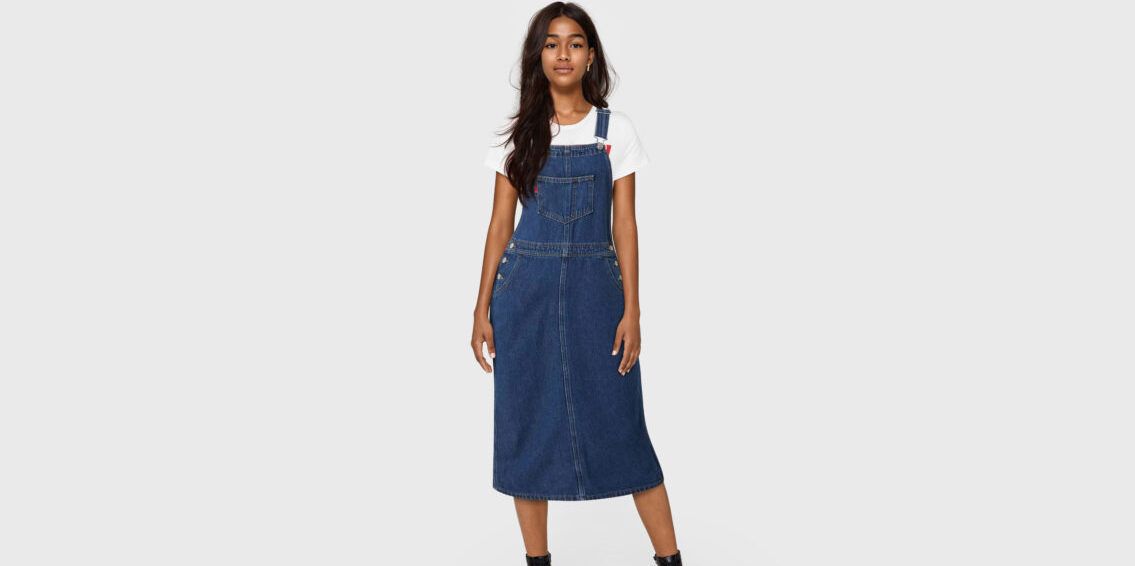 An AI-generated girl with deep brown skin and long black hair wears a mid-length denim dress and a white T-shirt