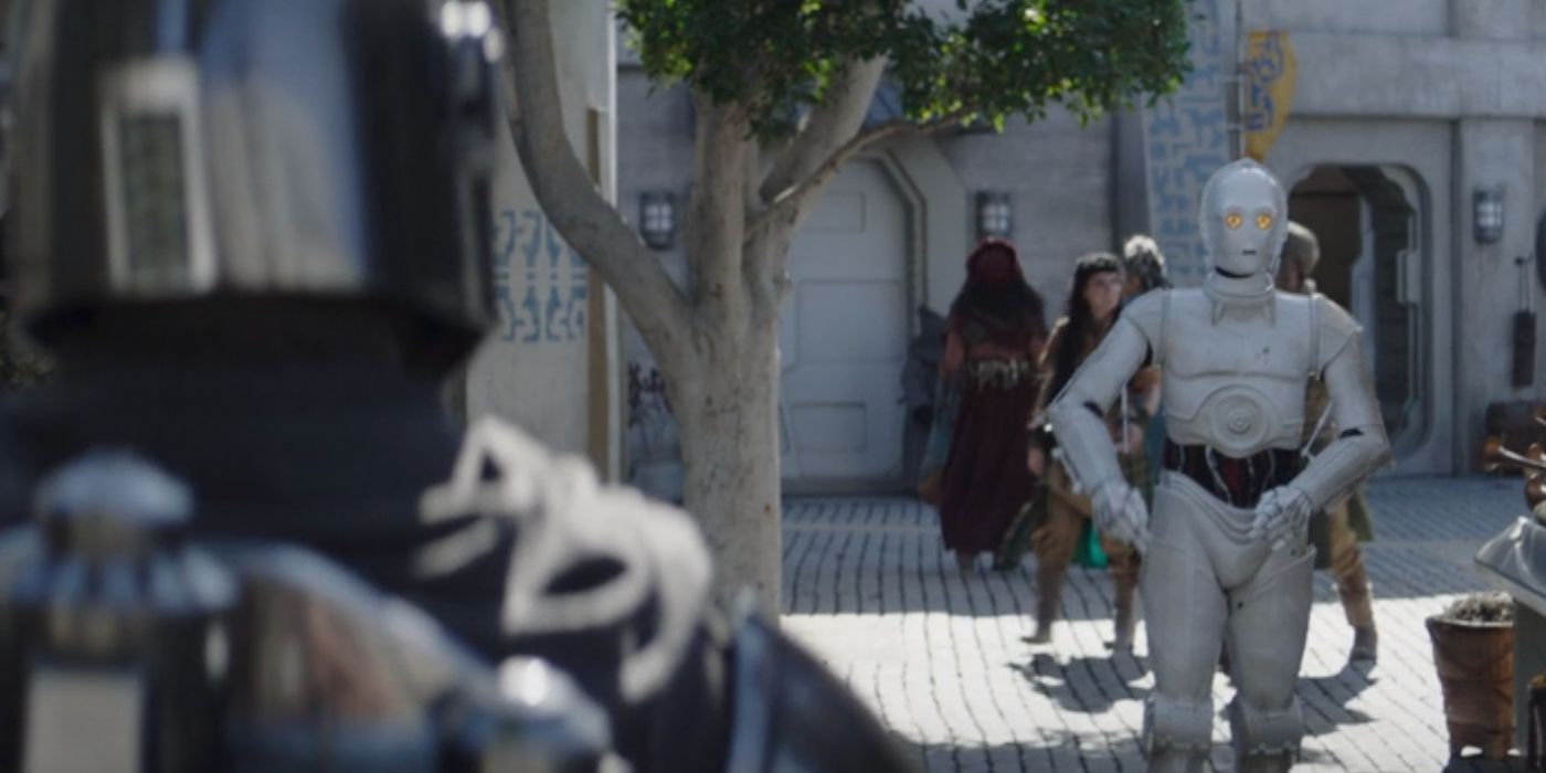 Din Djarin walking past a protocol droid on Nevarro in The Mandalorian Season 3
