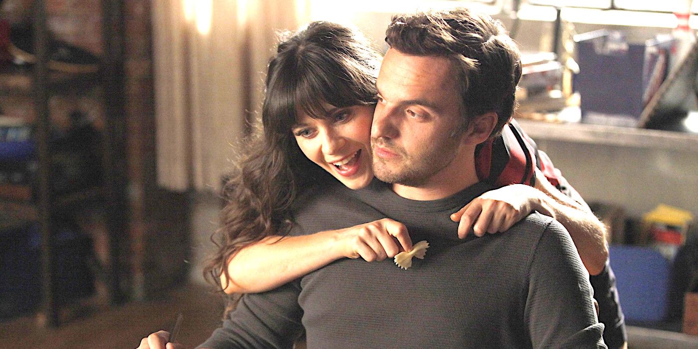 Zooey Deschanel as Jess in New Girl, Smiling and Embracing a Frowning Jake Johnson as Nick Miller, as He Sits at a Table Eating Pasta