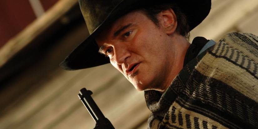Quentin Tarantino wearing a poncho and cowboy hat as he aims a gun upward in Sukiyaki Western Django