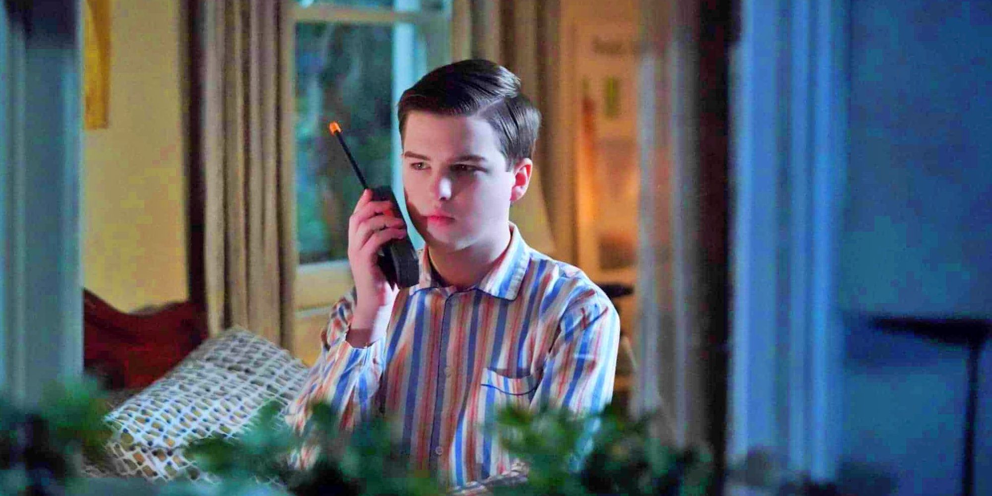 Sheldon holding a walkie-talkie in Young Sheldon season 6 in front of a window