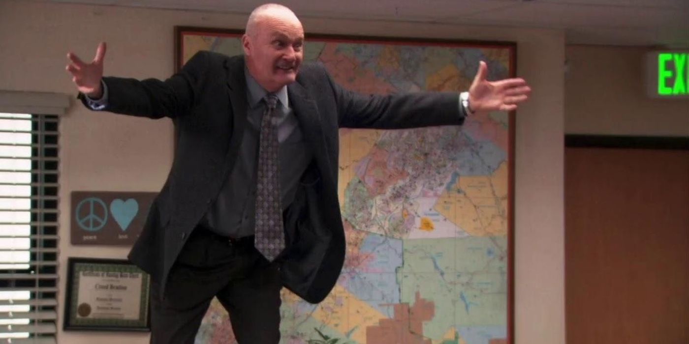 Creed standing on a desk with his arms open in The Office