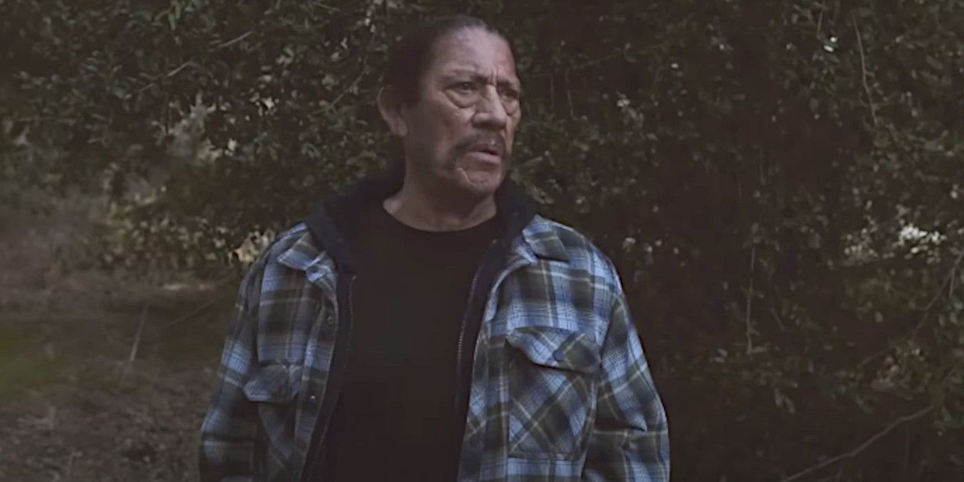 Danny Trejo in The Curse of Wolf Mountain wearing a flannel in the woods, looking mildly concerned