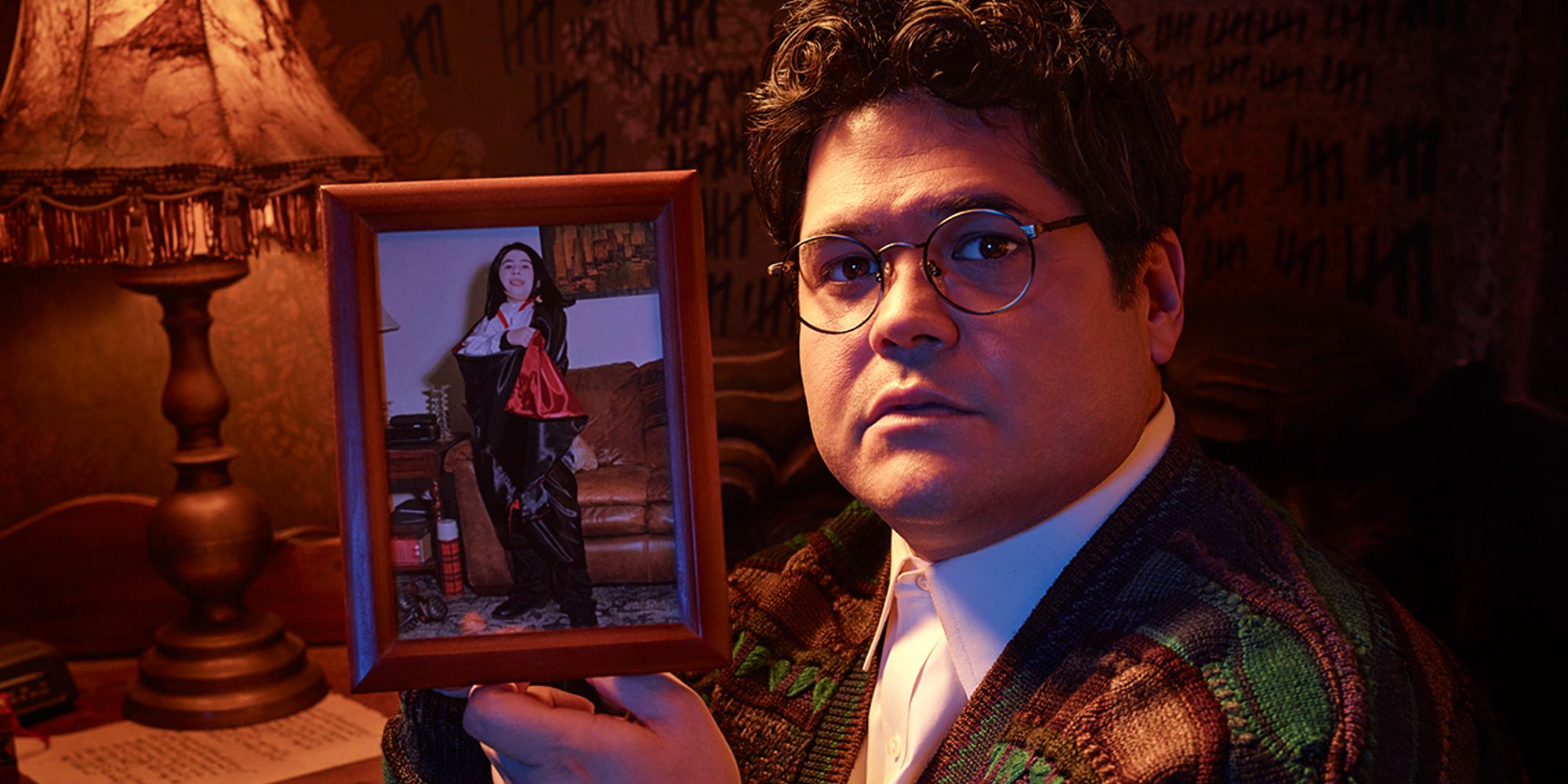 Harvey Guillen as Guillermo de la Cruz holding a framed photo in What We Do In The Shadows