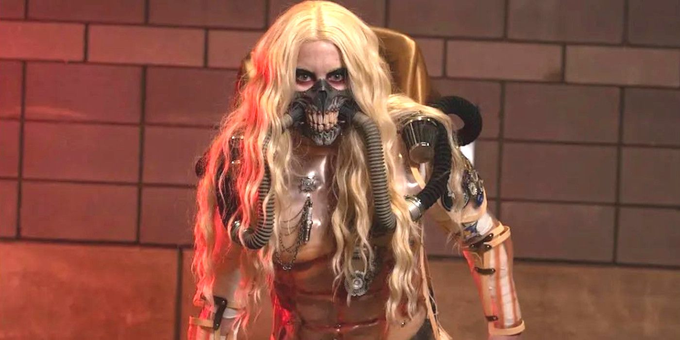 A cosplayer dresses up as Mad Max's Immortan Joe, glaring wildly while posing against a cinderblock wall